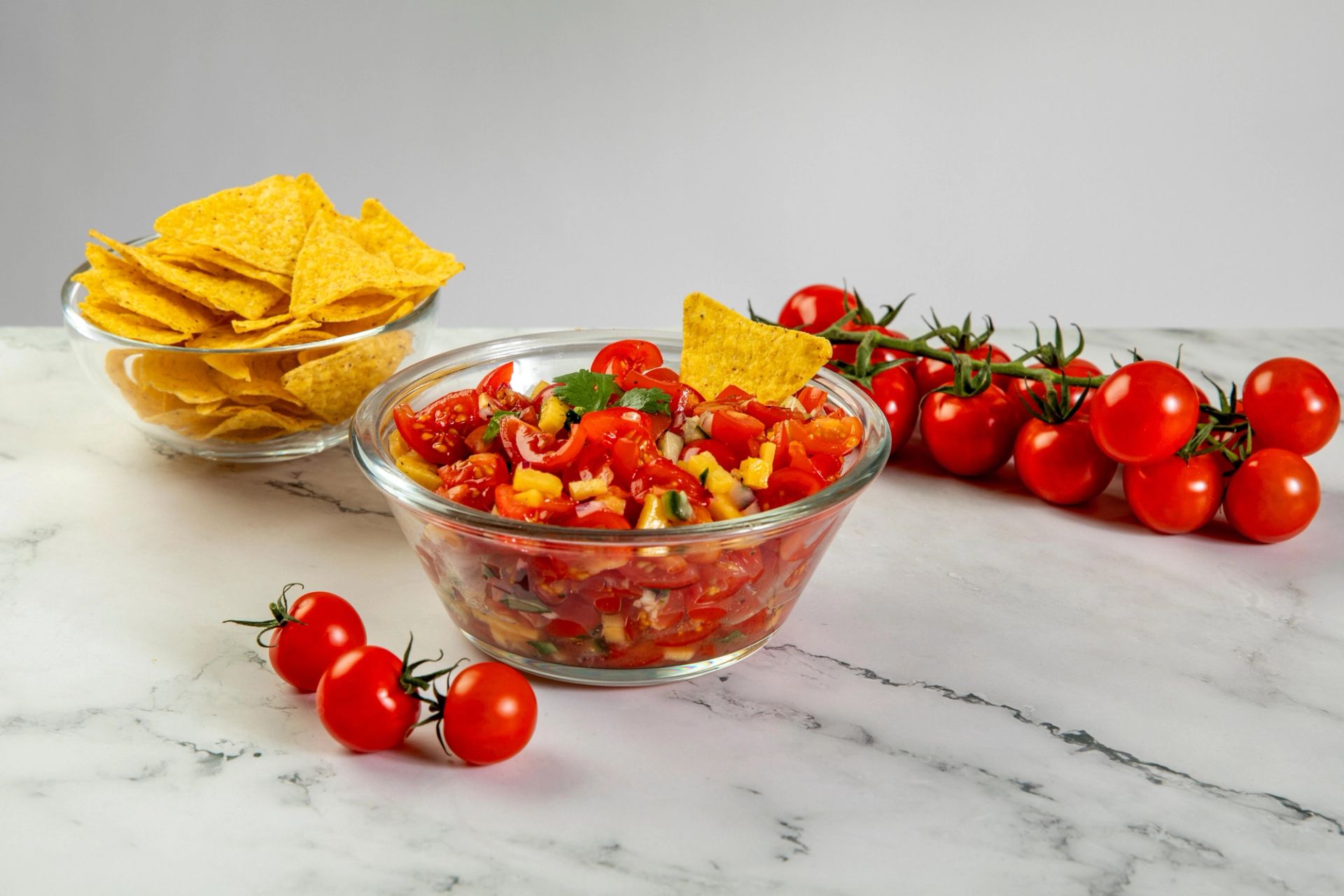 Tomatsalsa i en skål, tortillachips og tomater i bakgrunnen. 
