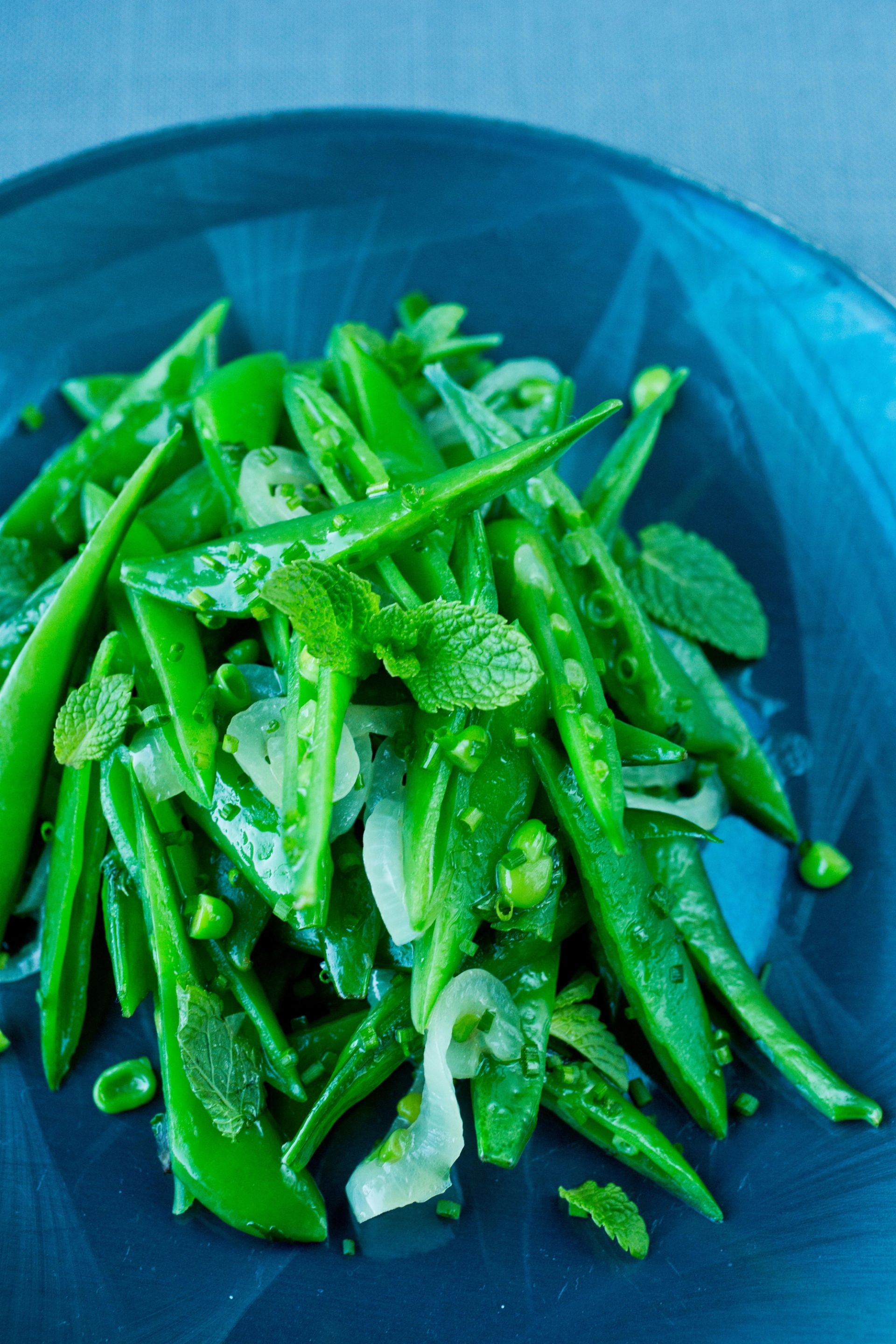 Grønn salat av sukkererter og erter blandet med tynne løkskiver og frisk sitronmelisse, servert i blå skål.