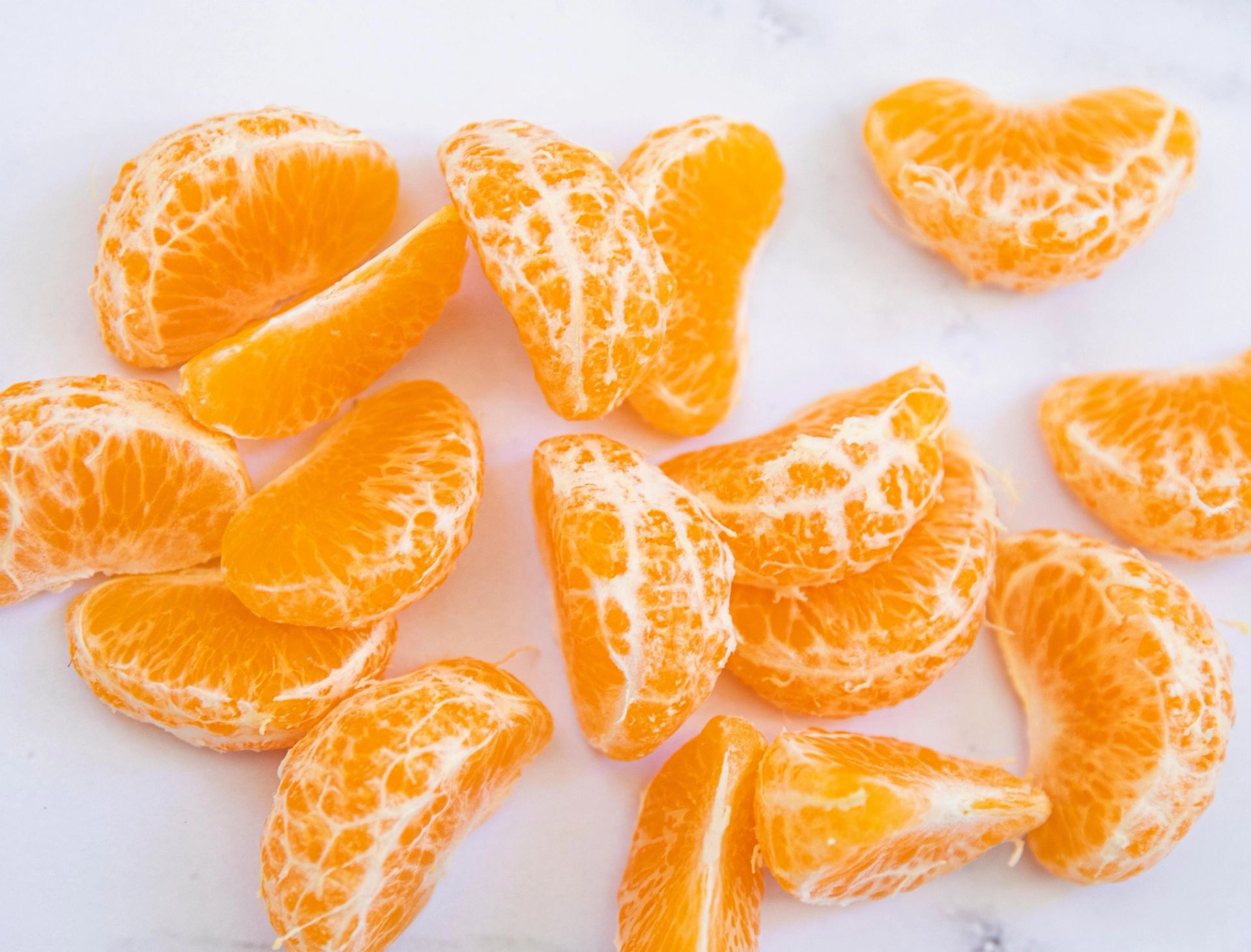Et nærbilde av flere skrelte mandarinsbåter som er spredt utover en lys, nøytral bakgrunn. Båtene er klare oransje med synlige hvite tråder fra fruktkjøttet som gir en naturlig og litt ujevn overflate.