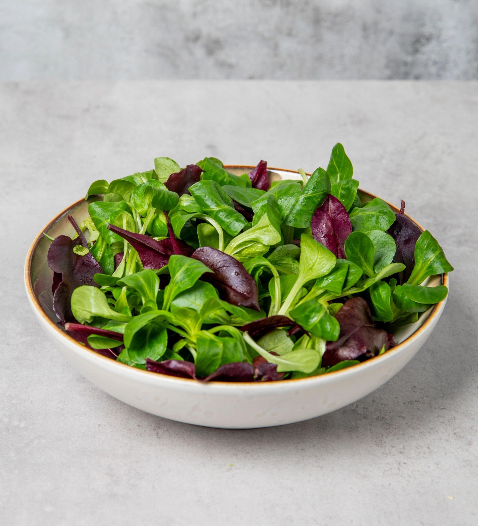 En bolle med grønn og mørkerød salat på en lys bordflate.