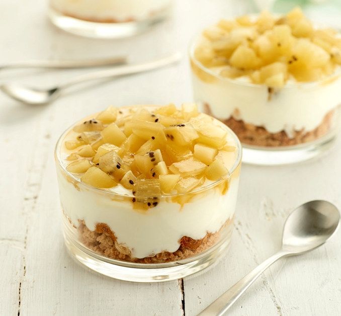 En frisk og lagvis dessert servert i glass, med en bunn av knuste kjeks, et lag med yoghurt og toppet med terninger av gul kiwi.