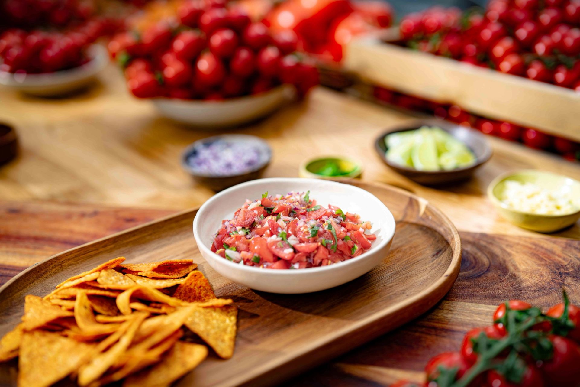 Skål med frisk tomatsalsa toppet med koriander, servert med tortillachips på et trebord, med tomater i bakgrunnen.