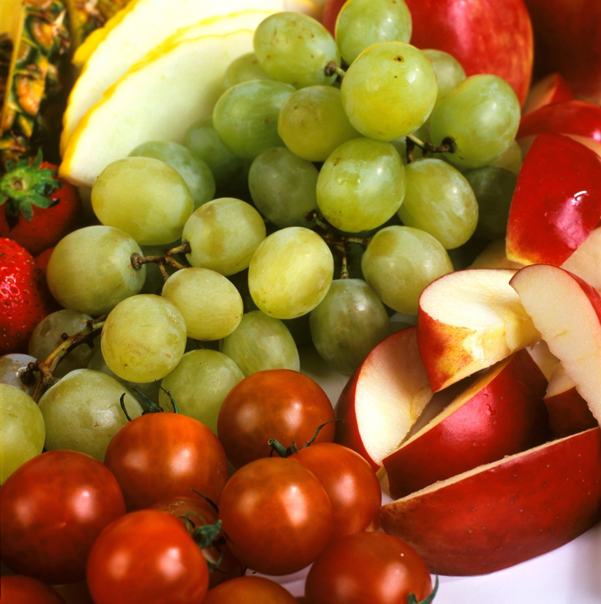 Utvalg av frukt med grønne druer i midten, omgitt av eplebåter og cherrytomater.
