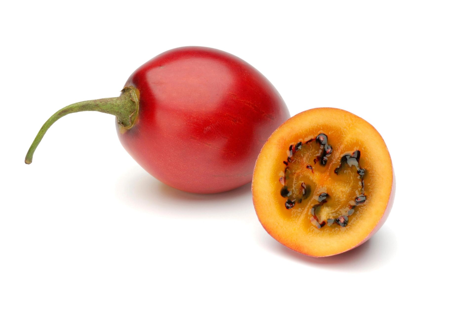 En tamarillo (tretomat), der én hel rød frukt ligger bak, og en delt frukt foran viser det gule-oransje fruktkjøttet med mørke frø i midten.