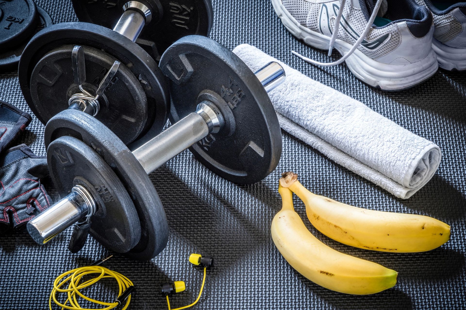 Treningsutstyr med manualer, hoppetau, håndkle og løpesko ligger på et treningsunderlag. Ved siden av utstyret ligger to bananer, som fremhever frukt som et enkelt mellommåltid før eller etter trening.