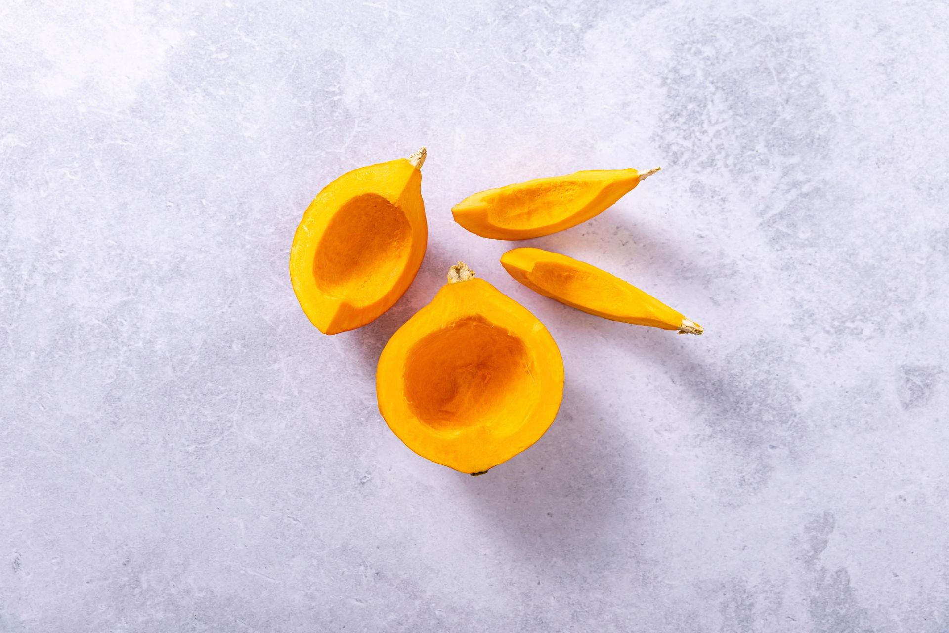 Halverte gule squash med uthult frøkammer, lagt på lys steinbakgrunn og fotografert ovenfra.