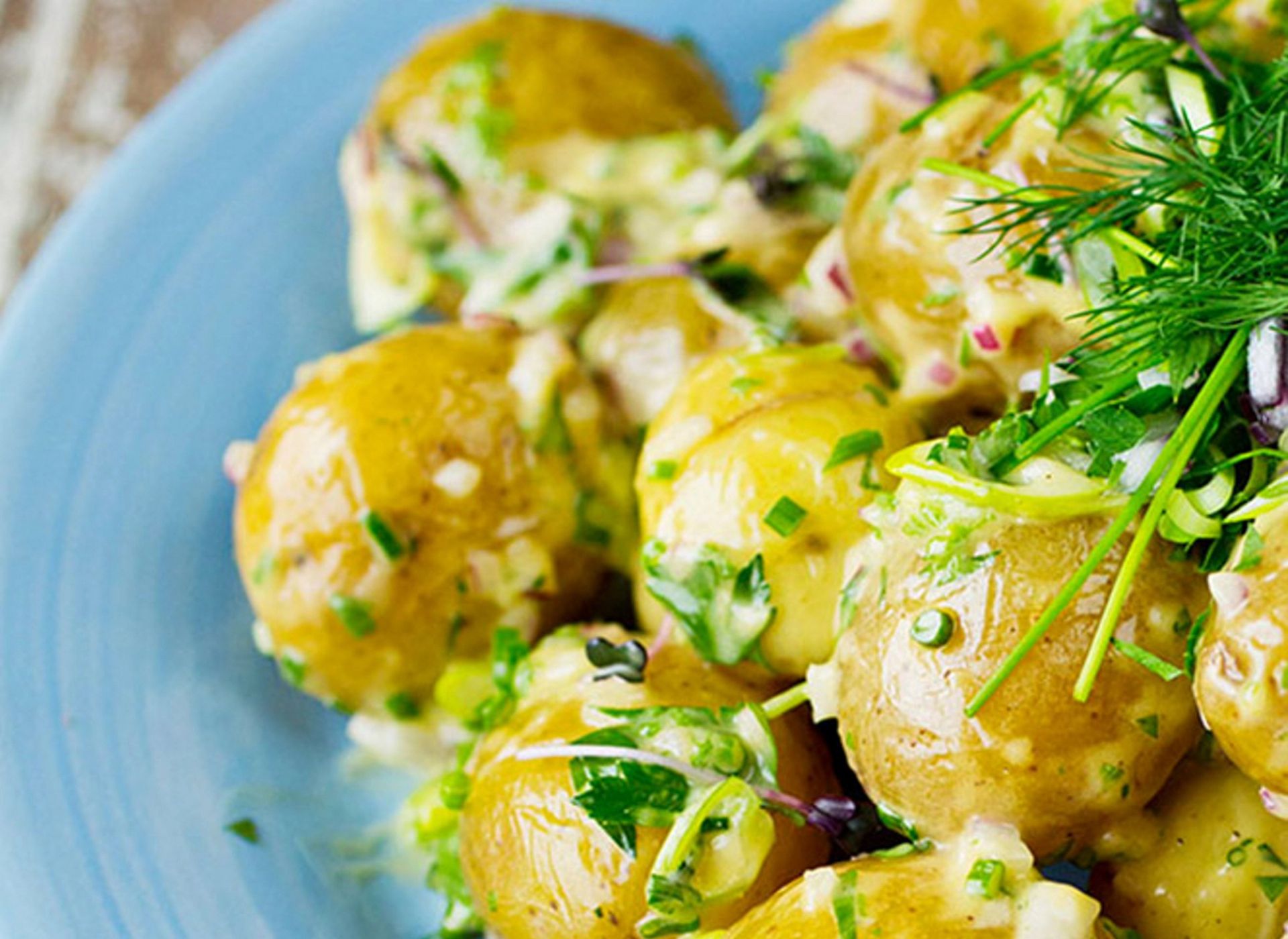 Nykokte poteter med sennepsdressing, gressløk, dill og rødløk på en blå tallerken.