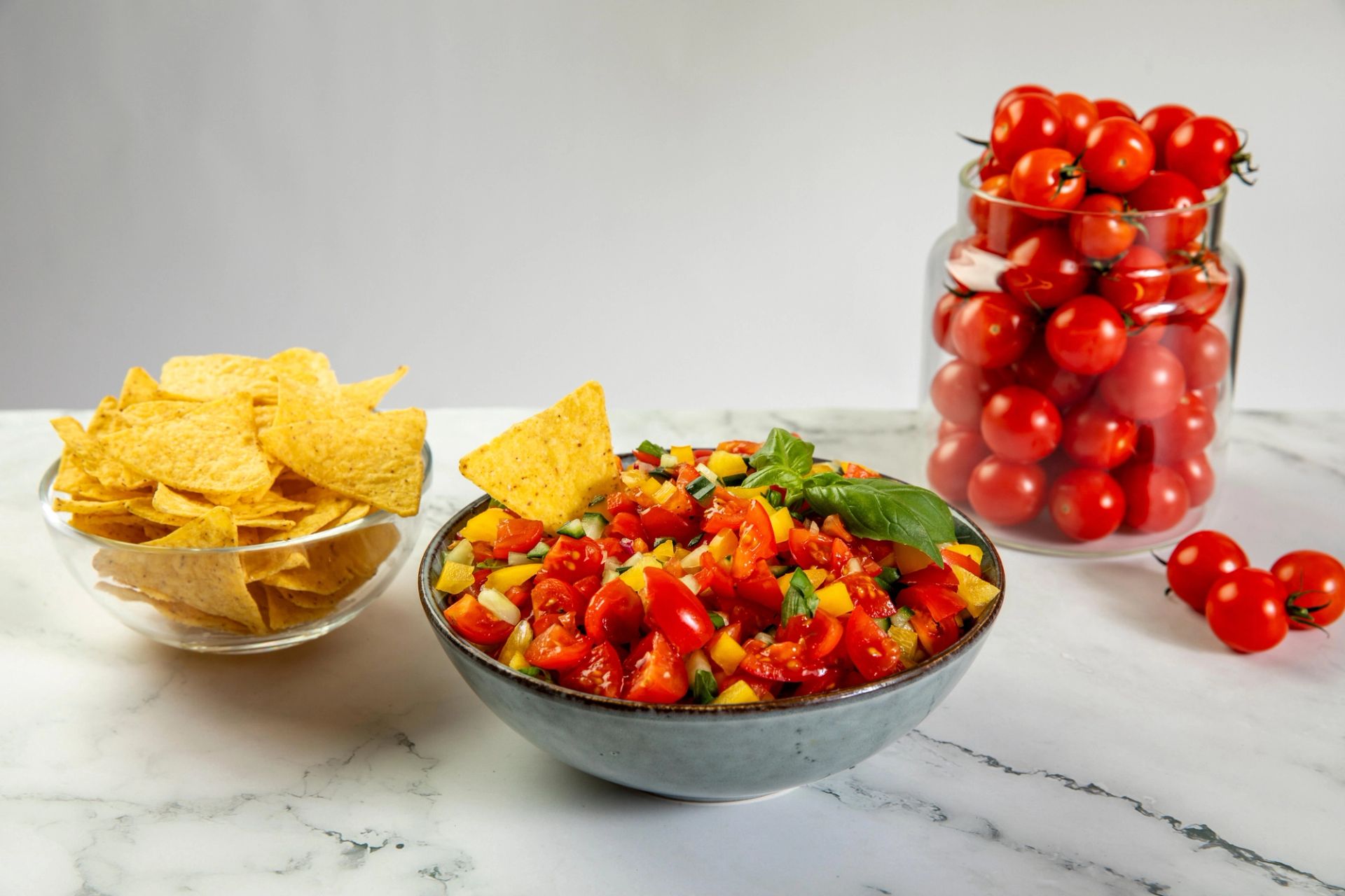 Fargerik tomatsalsa med cherrytomater og basilikum i en skål, servert med tortillachips og friske tomater.
