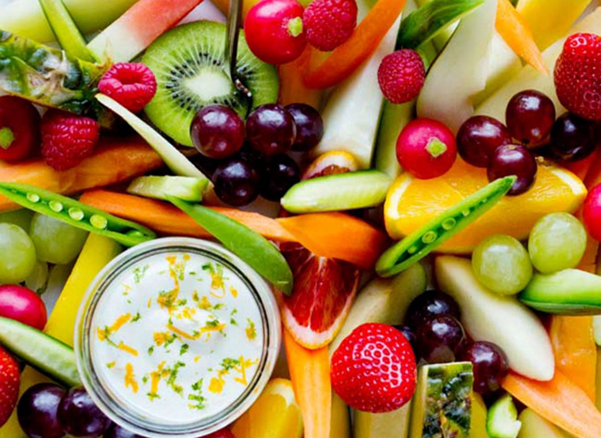 Fargerikt frukt- og grøntfat med oppskåret frukt, grønnsaker og kremet dipp i midten.