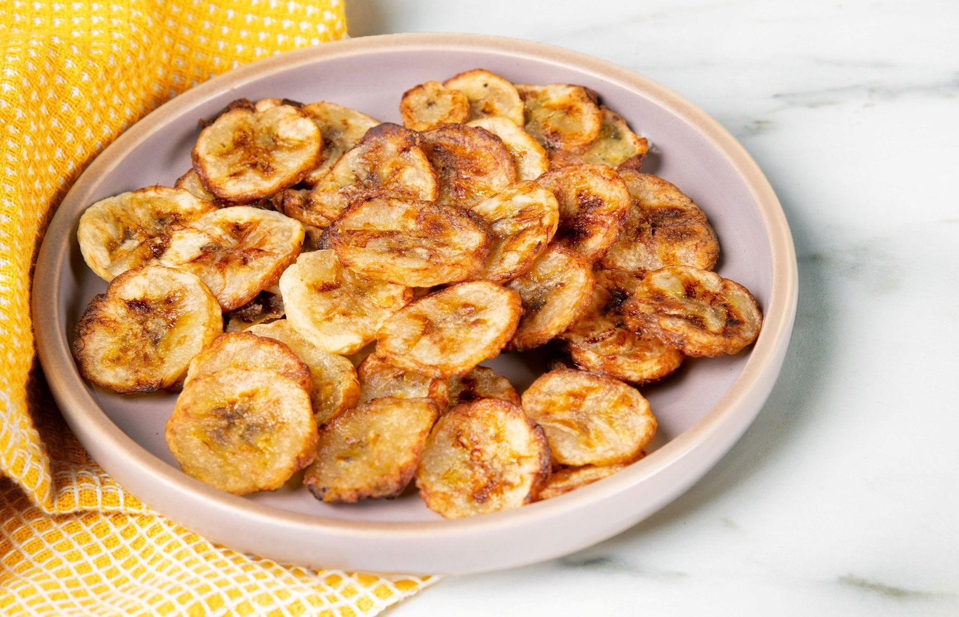Tynne skiver av banan stekt i airfryer til sprø bananchips, gyldne i fargen og klare til servering.