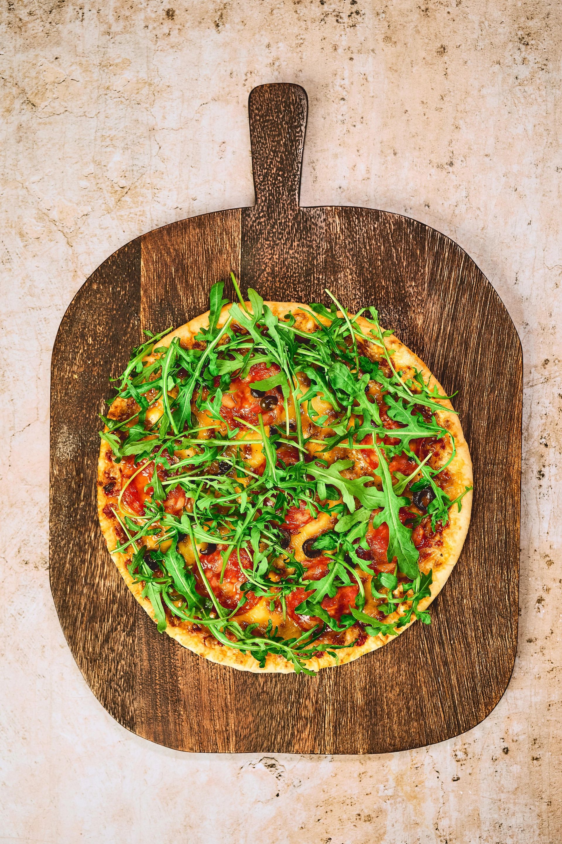 Pizza på trefjøl toppet med salat.