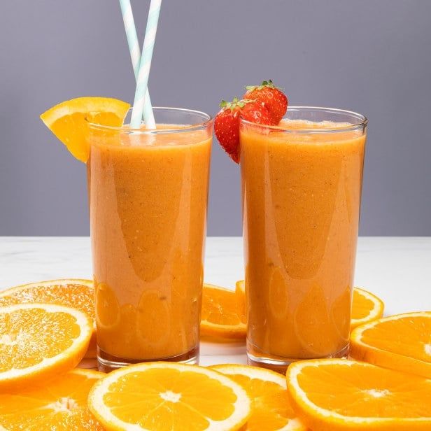 Frisk energismoothie med appelsin, jordbær og sitrus, servert i høye glass med ferske appelsinskiver rundt.