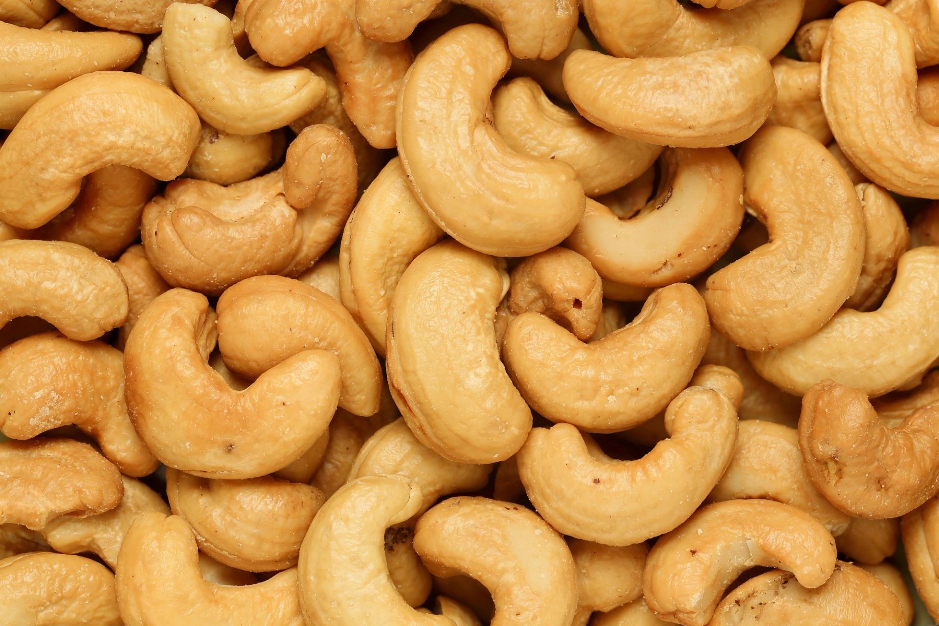 Nærbilde av cashewnøtter som ligger tett sammen, lysebrune og buede med glatt, lett blank overflate.