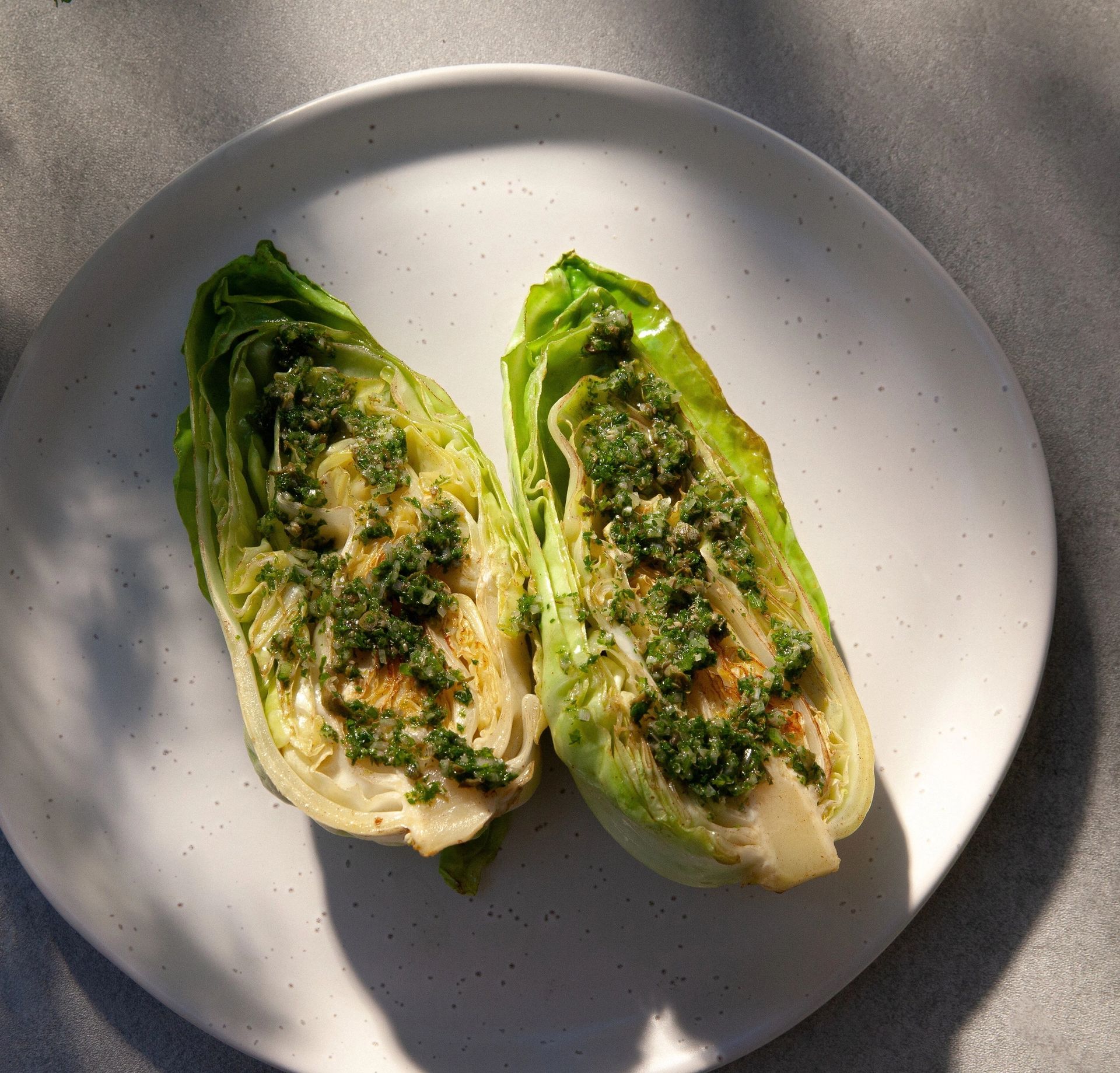 To halve spisskål med gyllenbrune stekemerker, toppet med en grønn salsa verde, servert på en lys tallerken.