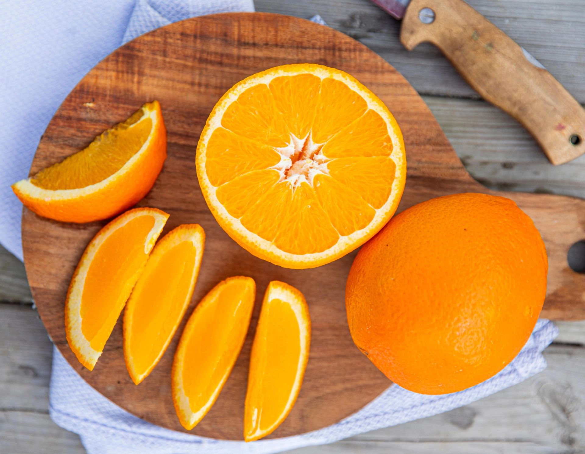Et helt og et halvt appelsin sammen med flere appelsinbåter lagt utover et rundt skjærebrett av tre, med frisk og saftig oransje farge.