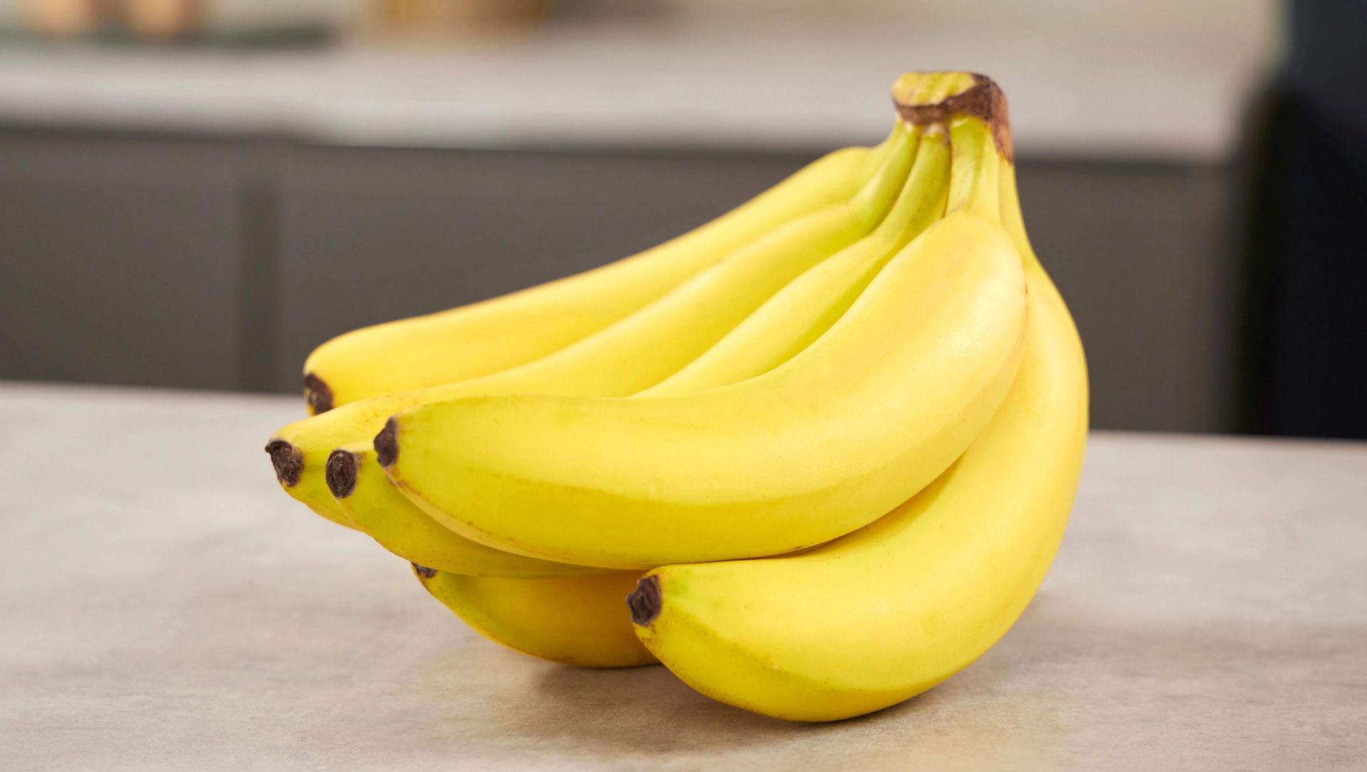 Et nærbilde av en klase med gule bananer på en beige kjøkkenbenk.