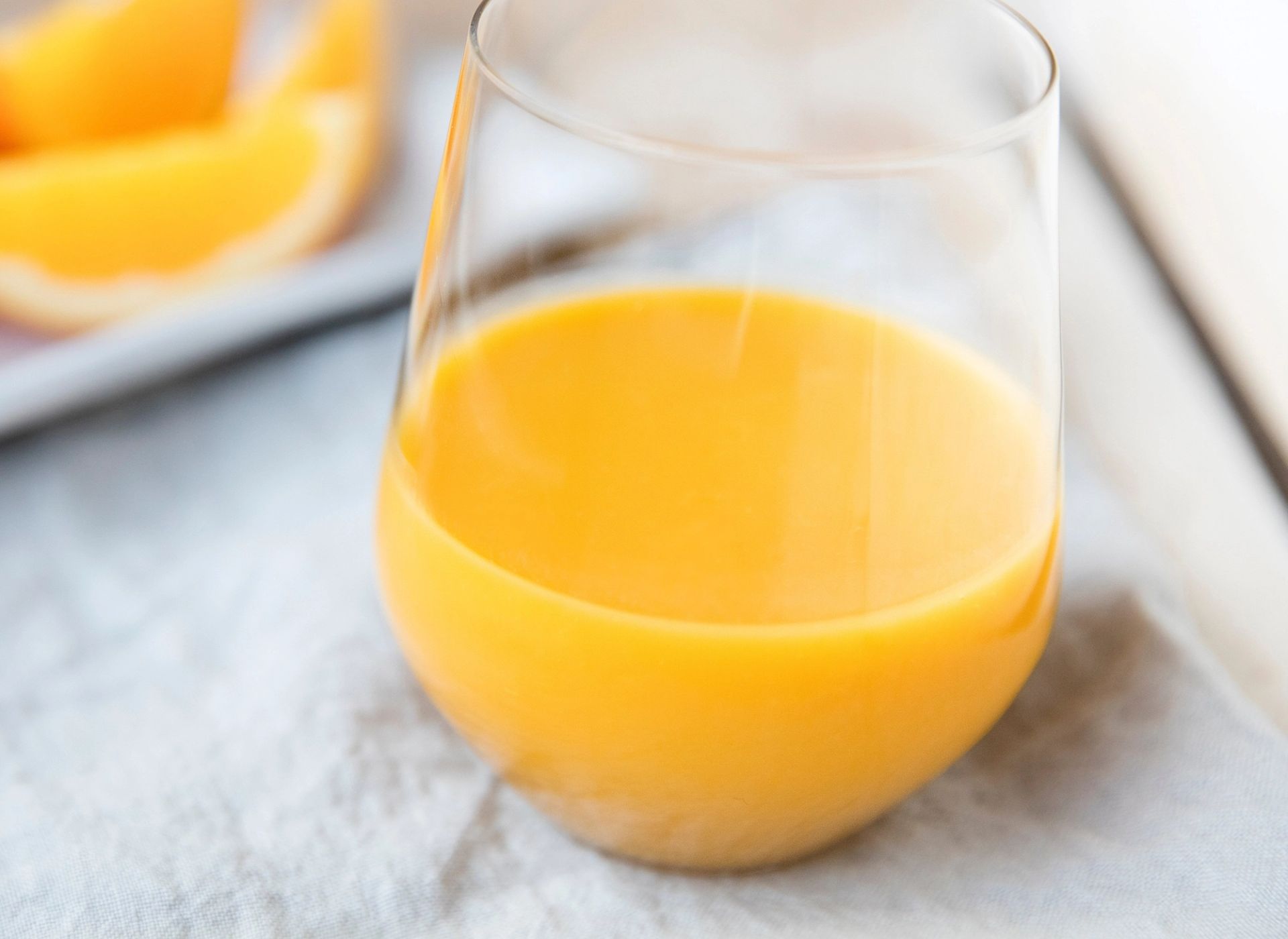 Kremet mangosmoothie i glass med myk, gyllen konsistens, fotografert på lys bakgrunn.