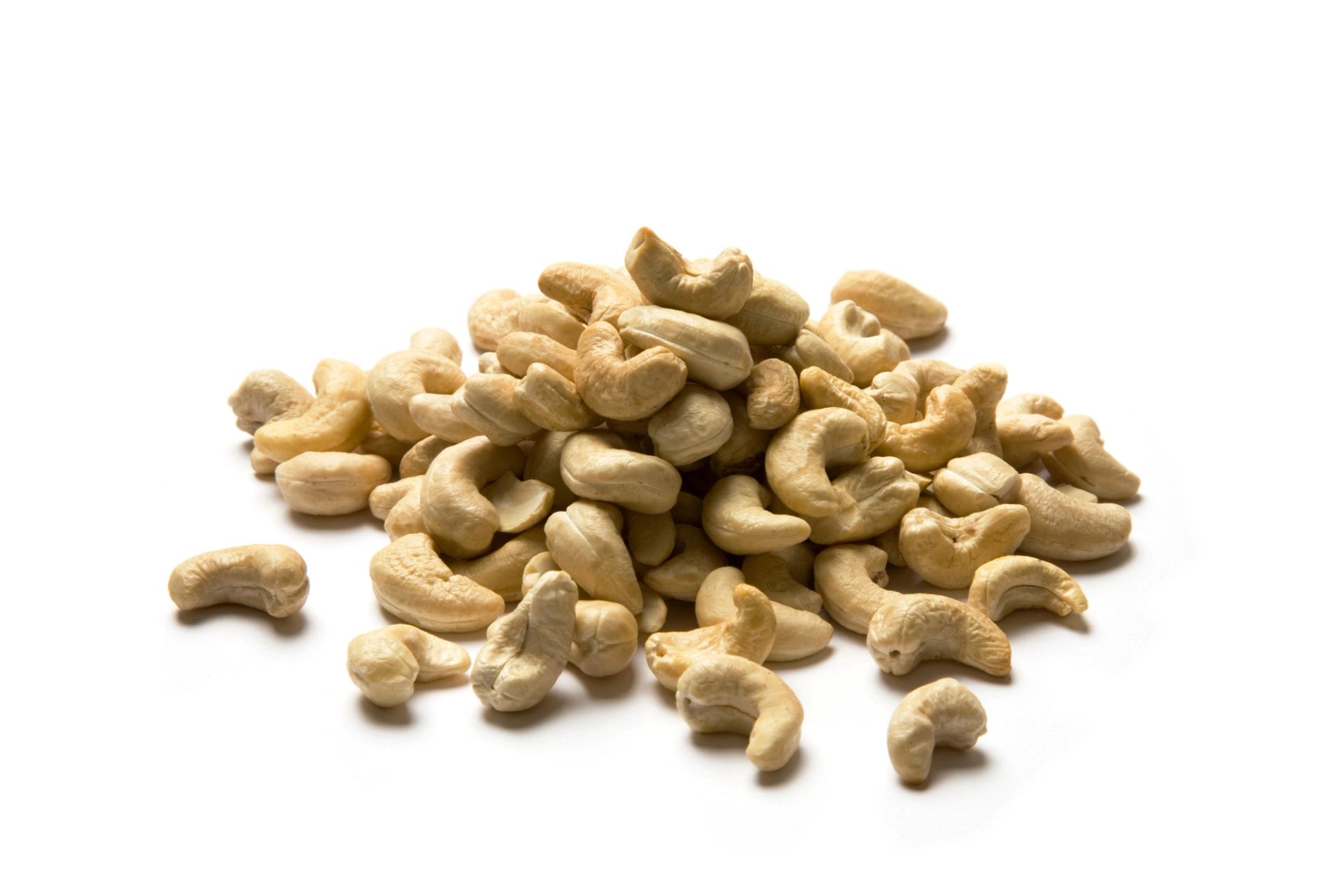 En liten haug med lyse, rå cashewnøtter ligger spredt på en hvit bakgrunn. Nøttene er buede og ujevnt formet, med en matt, kremfarget overflate.