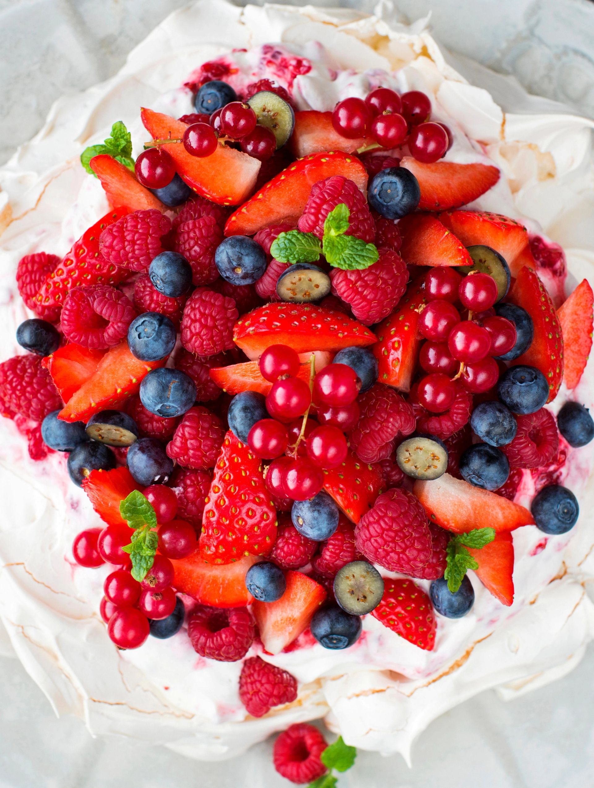 En pavlova toppet med en miks av friske bær, inkludert jordbær, bringebær, blåbær og rips, pyntet med noen mynteblader.