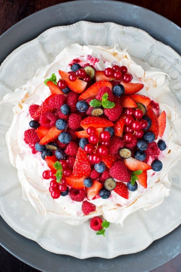 Pavlova med sprø marengs, pisket krem og ferske bær som jordbær, bringebær, blåbær og rips. Servert på et pent kakefat.