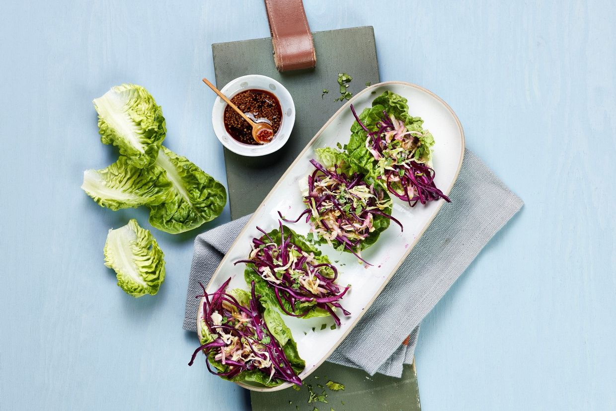 Hjertesalat fylt med en fargerik blanding av finsnittet rødkål og hodekål, servert på et avlangt fat. Ved siden av står en liten skål med mørk dressing og treskje, plassert på en mørkegrønn fjøl.