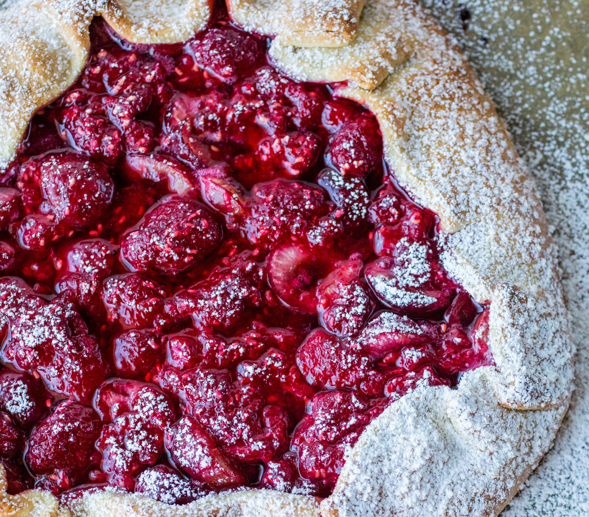En rustikk terte eller galette med lett stekte kanter og fyll av bringebær og moreller. Hele terten har et dryss av melis. 