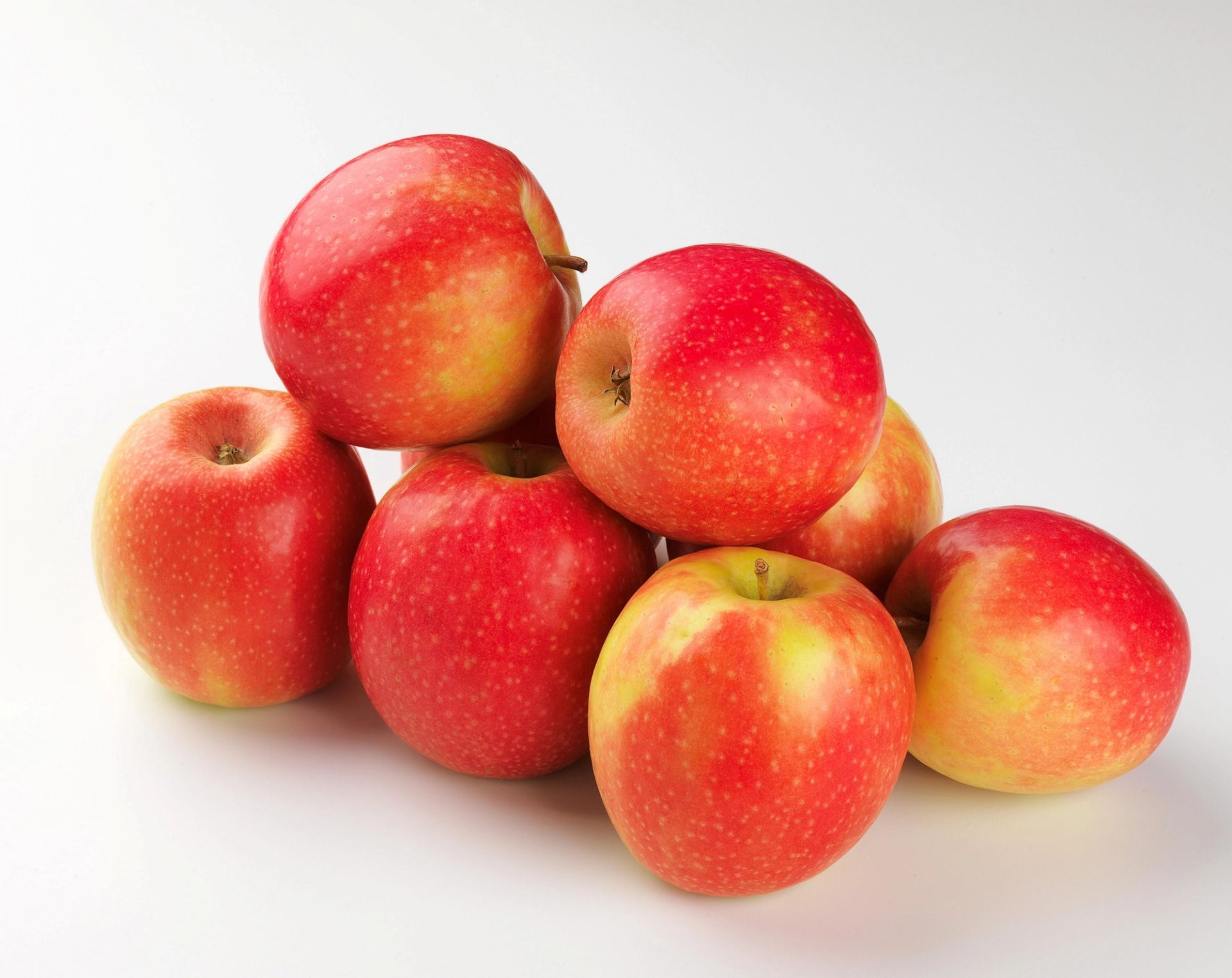 Flere røde epler stablet i en liten haug på hvit bakgrunn.