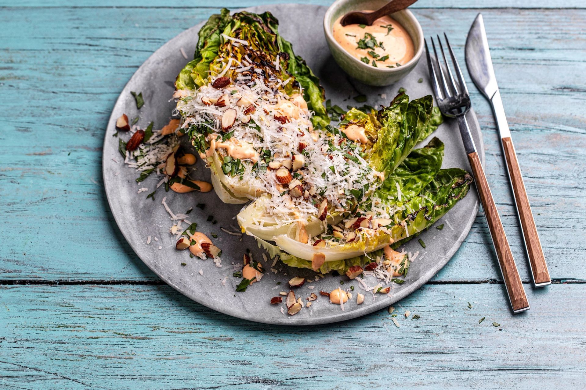 Grillet hjertesalat med sprø kanter og tydelige grillmerker, toppet med ristede mandler, revet parmesan og kremet chilimajones – servert på tallerken med dressing ved siden av.