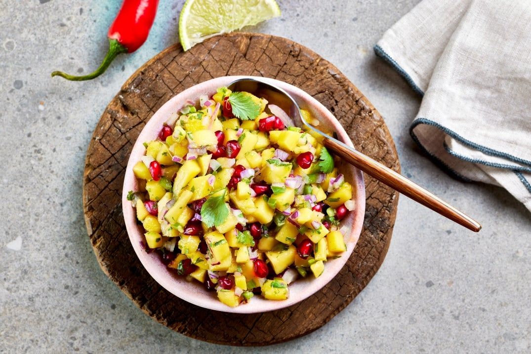 Skål med frisk mangosalat sett ovenfra, med terninger av mango, granateplekjerner, rødløk og koriander.