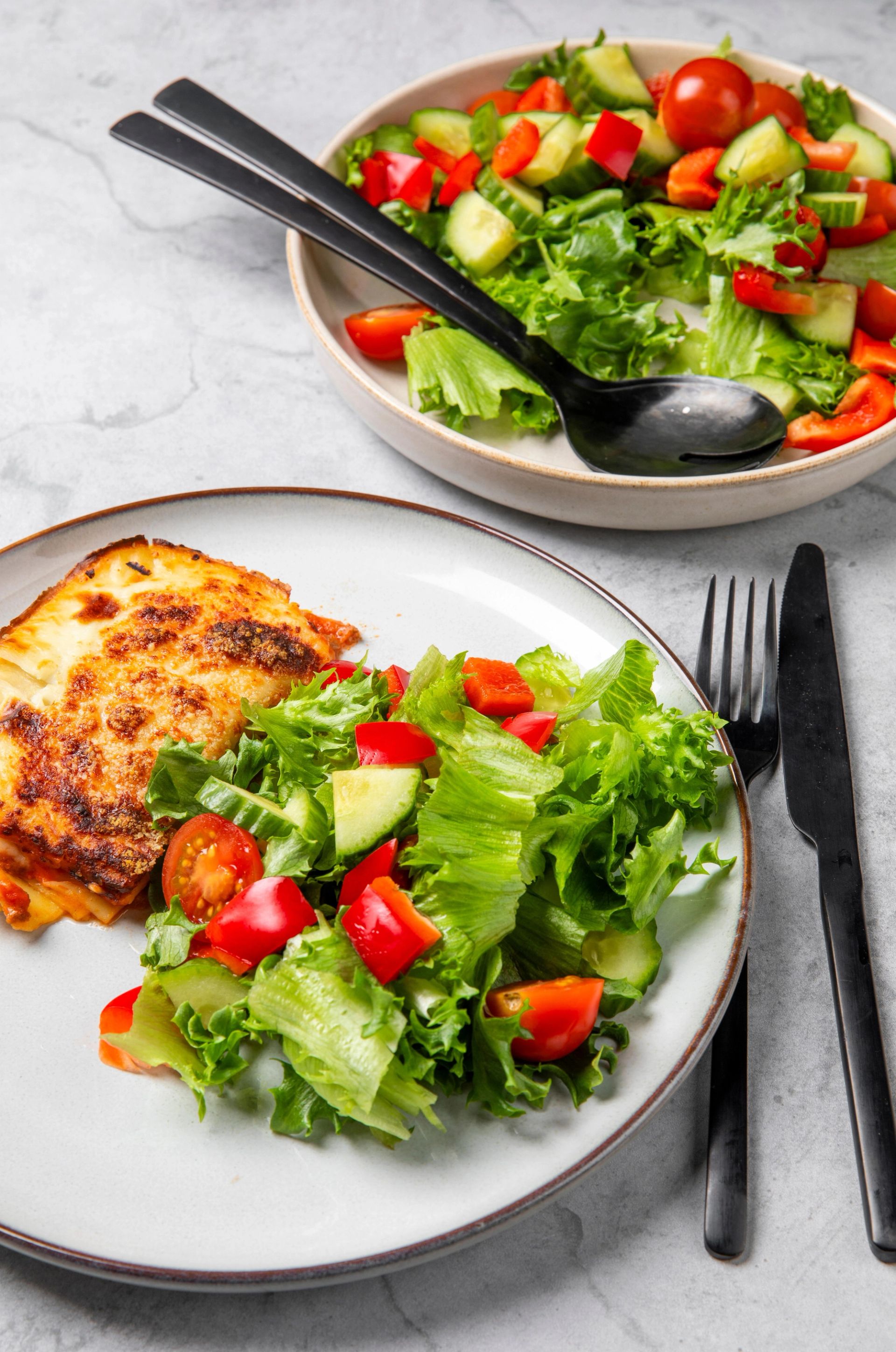 Tallerkener med crispisalat blandet med tomat, paprika og agurk, servert sammen med en varmrett på en av tallerkenene. Bestikk ligger ved siden av, og en større bolle med samme crispisalat står i bakgrunnen.