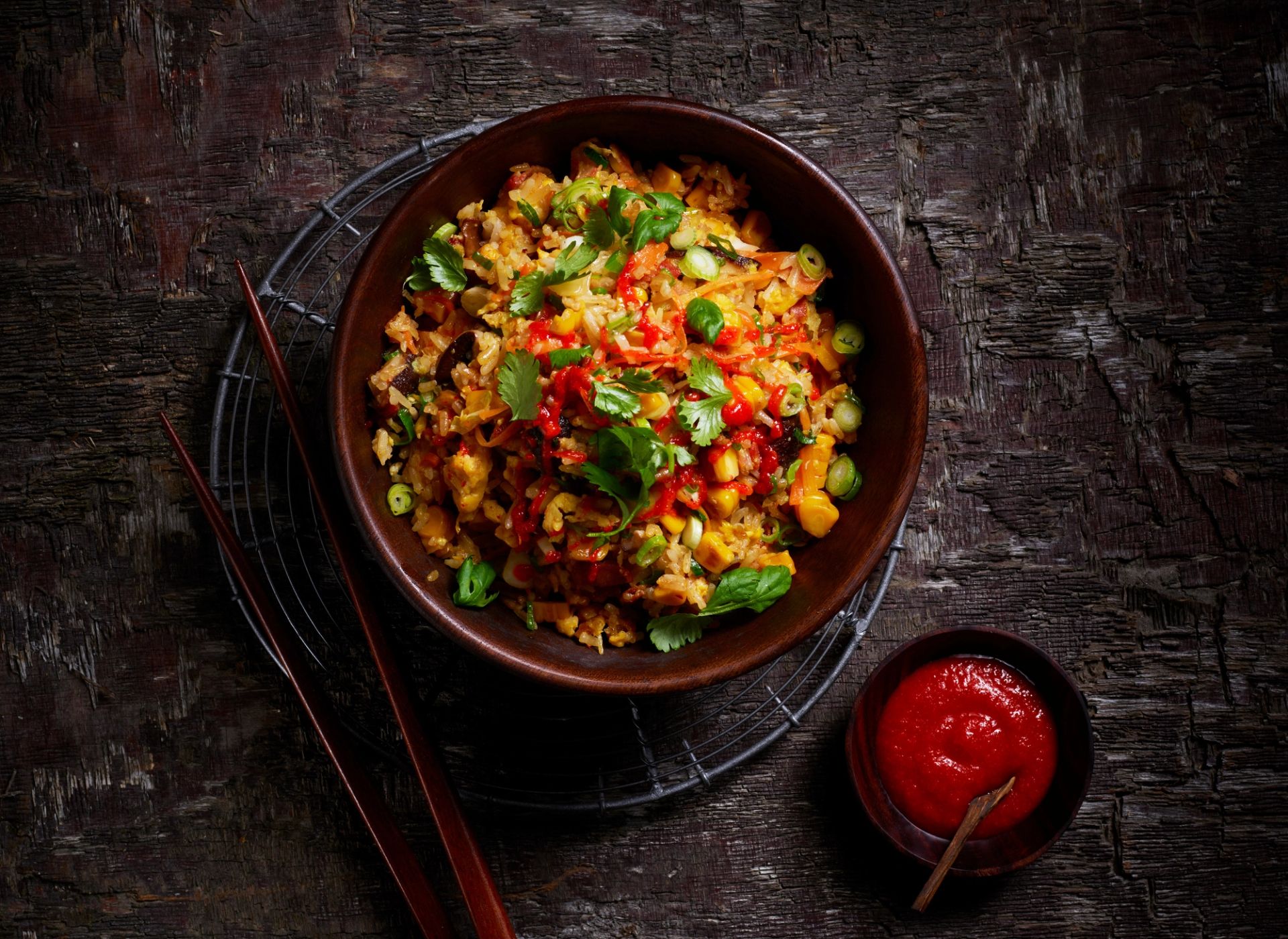 Stekt ris med kimchi toppet med koriander, vårløk og chilisaus i rustikk bolle med spisepinner.