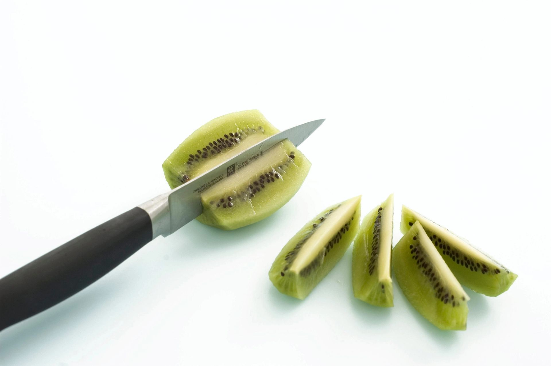 Skrelt kiwi som skjæres i båter med en kniv, plassert på hvit bakgrunn.