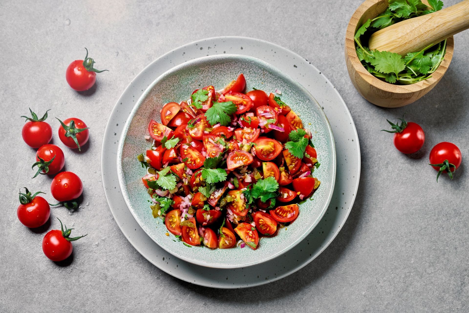 Skål med frisk tomatsalat laget av halverte cherrytomater, finhakket rødløk og koriander, servert på en lys tallerken. 