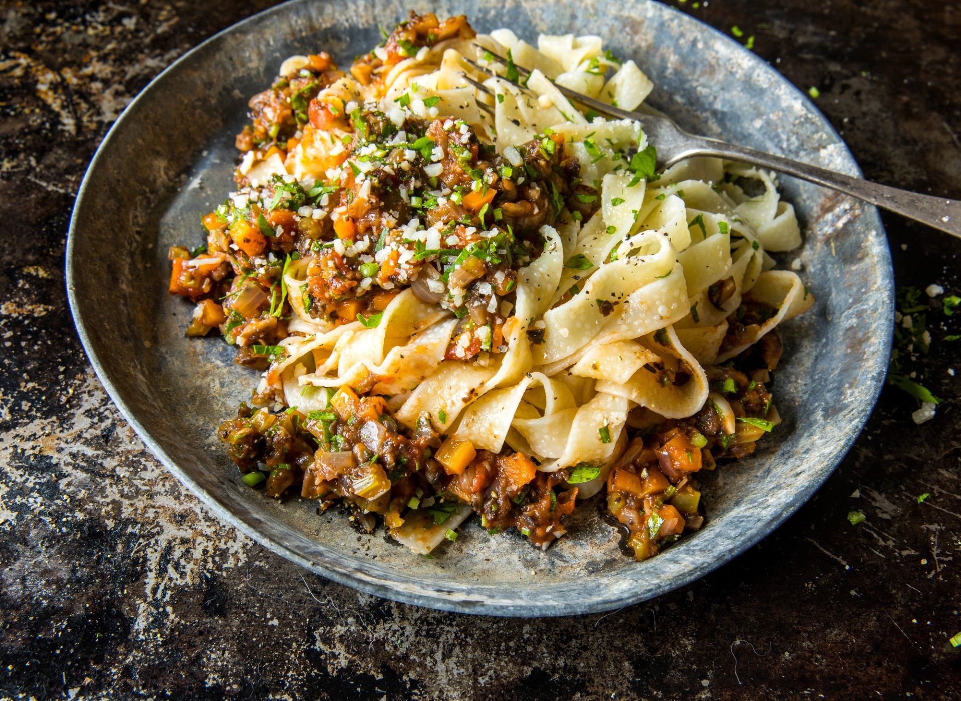 Pasta bolognese i keramisk tallerken  med grønnsaker, toppet med revet parmesanost.