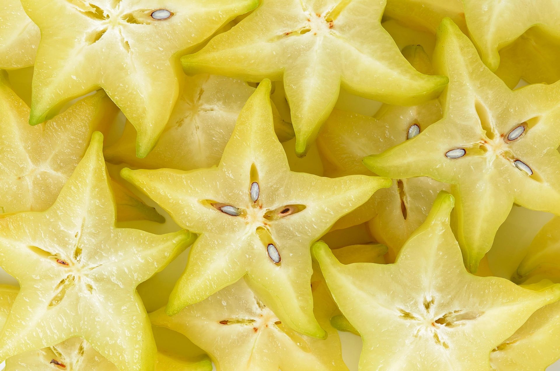 Nærbilde av skiver av stjernefrukt (carambola), der de gule fruktbitene danner tydelige stjerneformer. Den saftige fruktkjøttet er lyst gult, med små brune frø synlig i midten av noen skiver.