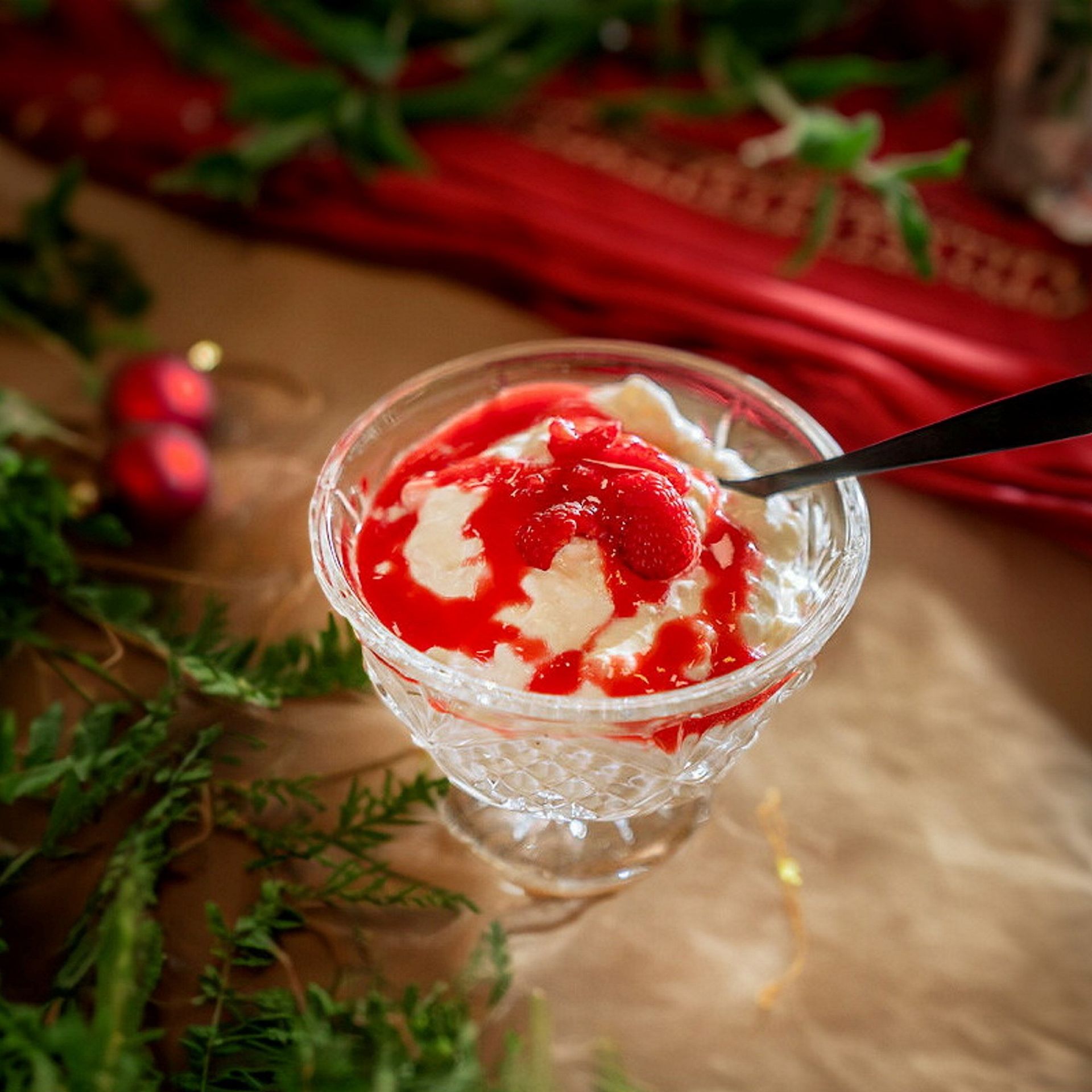 Klassisk riskrem til jul servert i glass, toppet med rød saus og friske bringebær.