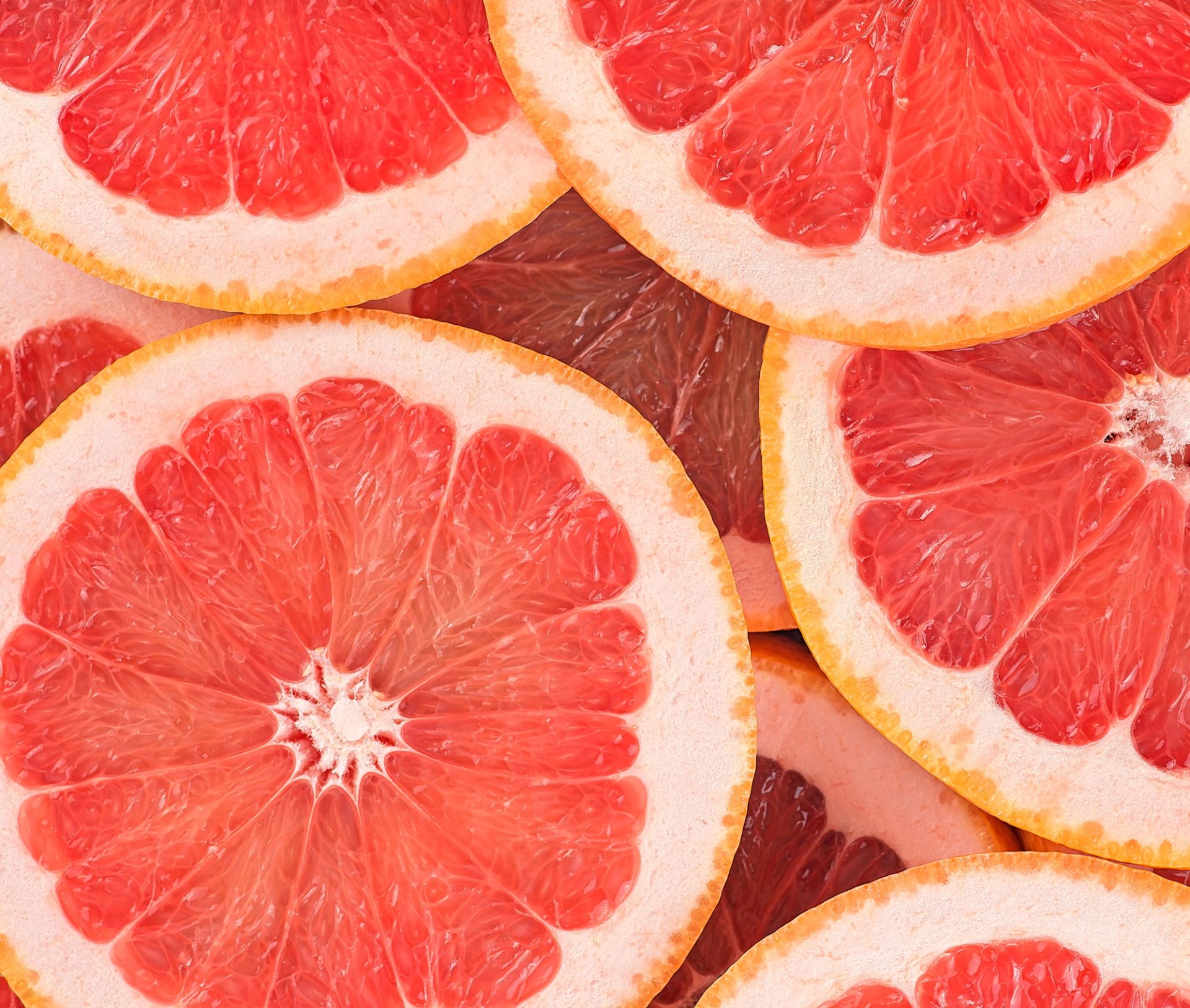 Flere overlappende skiver av rosa grapefrukt fyller hele bildet, med tydelige segmenter og lys gulskjær i skallet