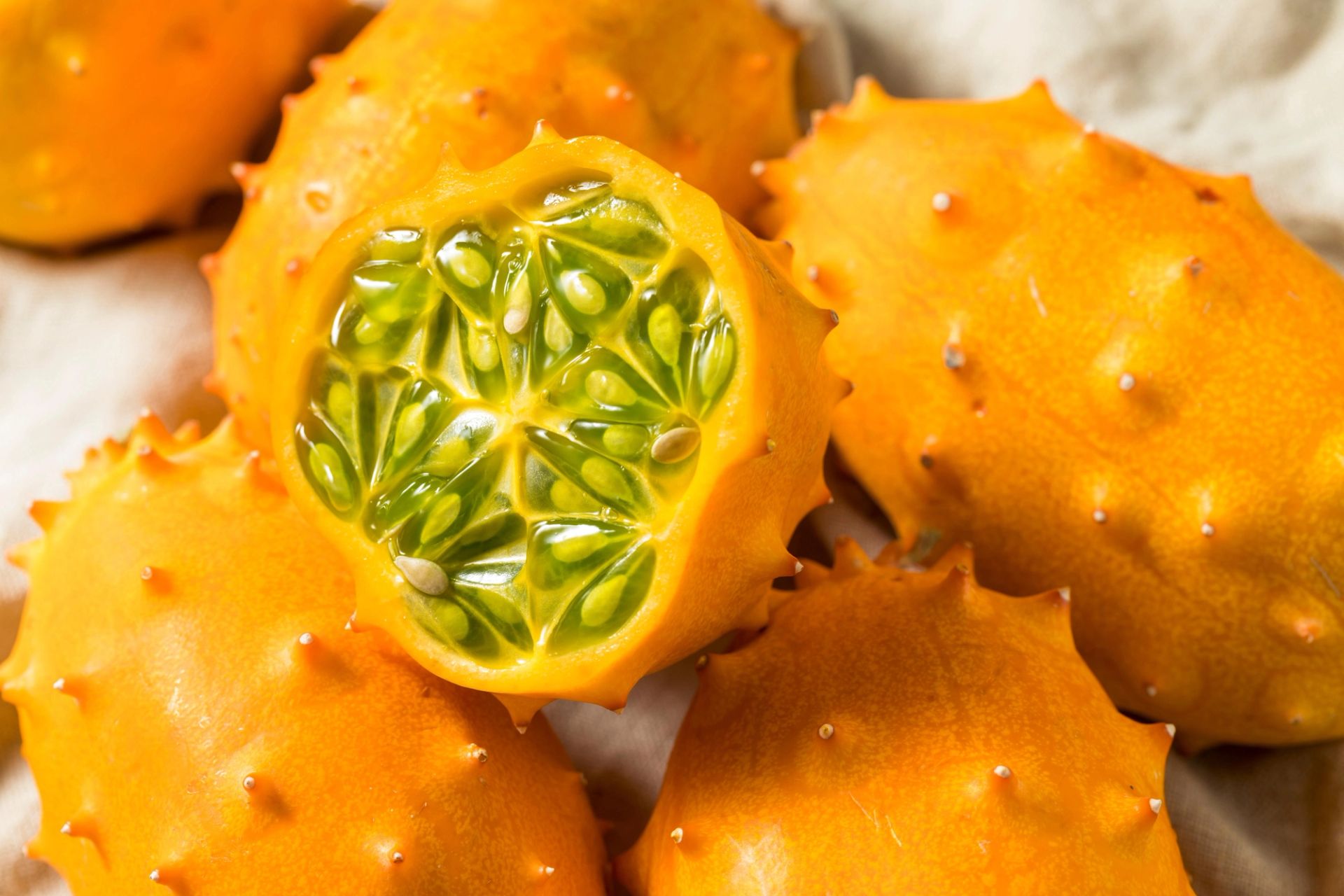 Halvert kiwano (hornmelon) med grønt, geléaktig fruktkjøtt og frø, omgitt av hele piggete frukter.