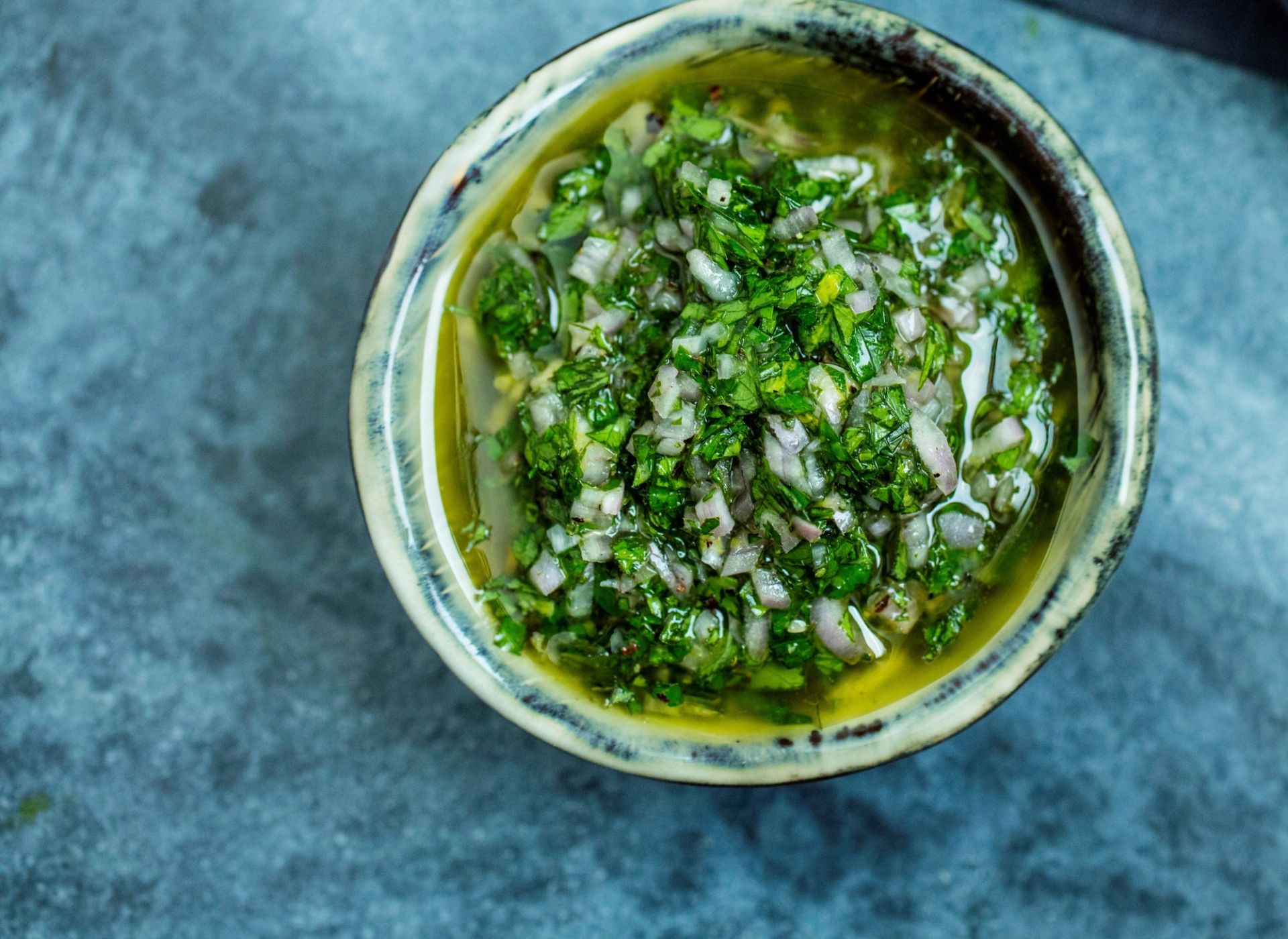 Salsa verde med finhakket persille, sjalottløk og olivenolje i en rustikk keramikkskål på en grå steinplate.