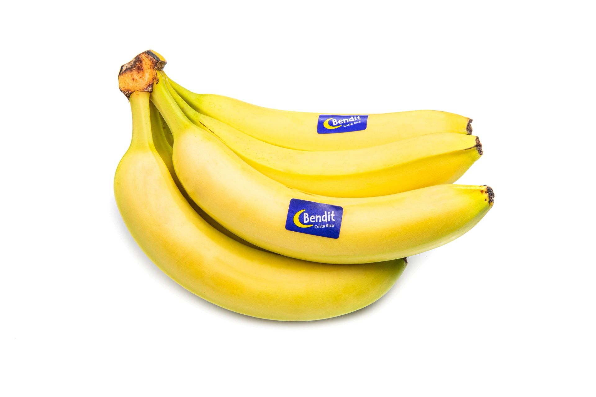  En bunt med gule bananer, tre stykker, med blå og gule Bendit‑klistremerker på, liggende mot en hvit bakgrunn.