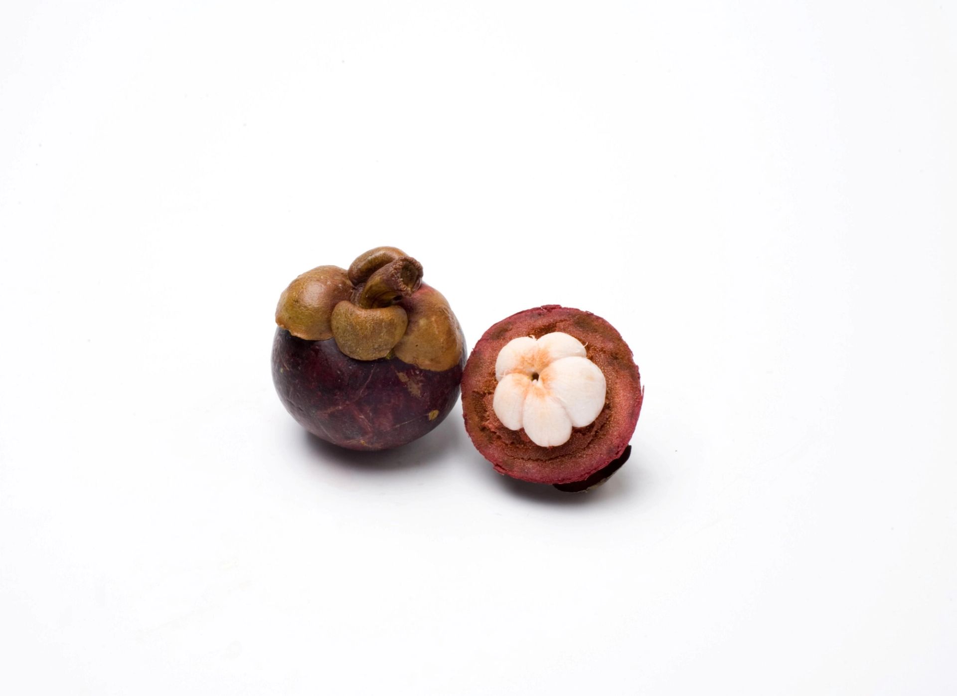 En hel og en halvert mangostan, der den halverte viser hvite, segmenterte fruktdeler inni det mørklilla skallet