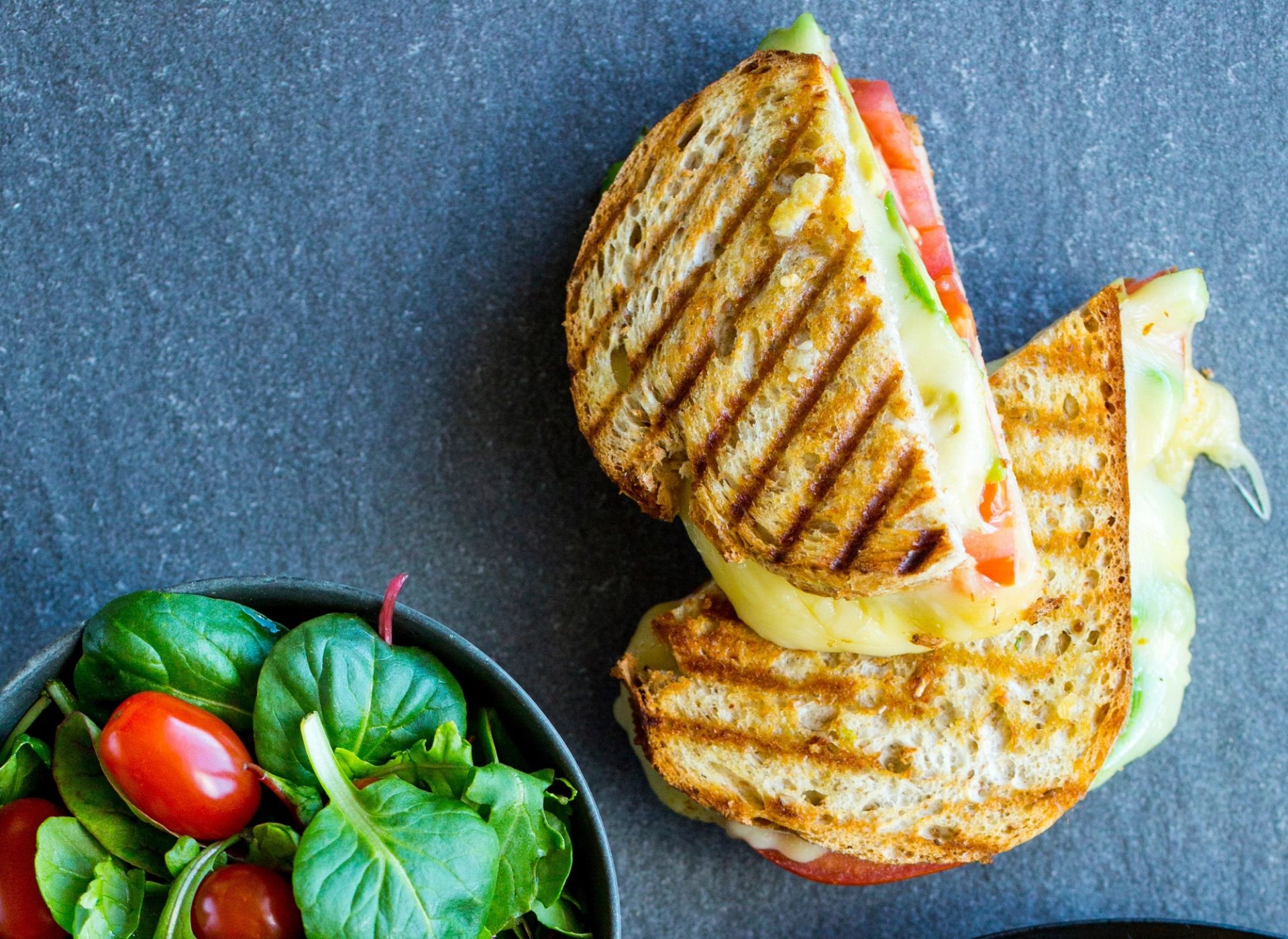 Grillet sandwich med smeltet ost, plommetomat og avokado, servert med frisk grønn salat.