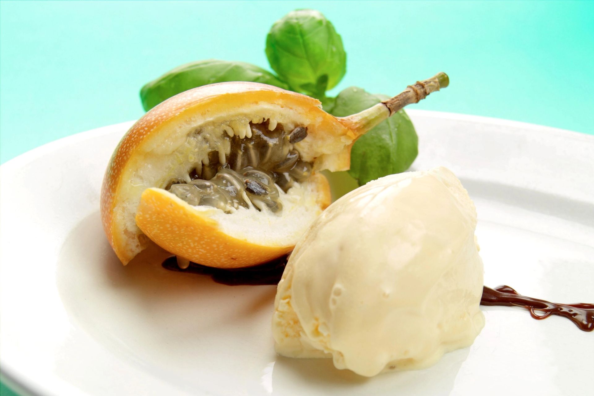Halvert granadilla med synlig fruktkjøtt og frø, servert med en kule vaniljeis og friske grønne blader på en hvit tallerken.
