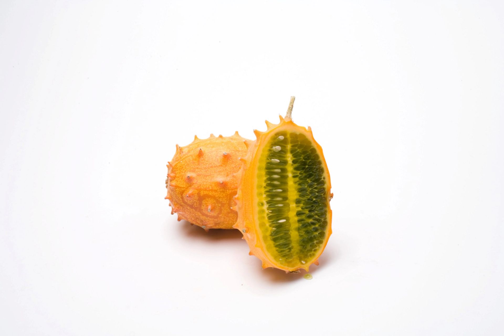 To kiwano-frukter, én hel og én delt i to som viser grønt, geléaktig fruktkjøtt på hvit bakgrunn