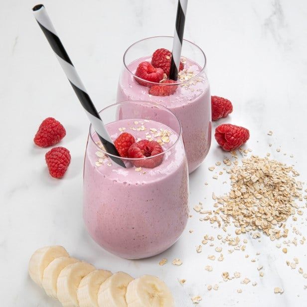 Kremet frokostsmoothie i glass med bringebær og havregryn, toppet med friske bær, fotografert på lys bakgrunn.