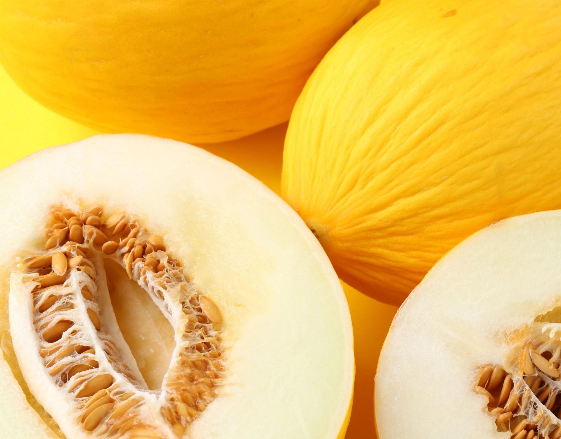 Gul melon (honningmelon), både hel og delt i to, som viser lyst fruktkjøtt og kjerner.