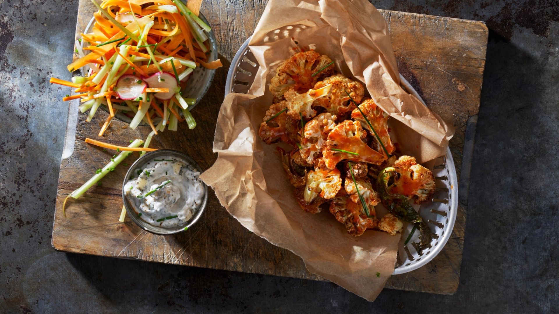Ovnsbakte blomkålbuketter i en bolle med bakepapir, servert med kremet dipp og frisk råkostsalat på et rustikt trebord.
