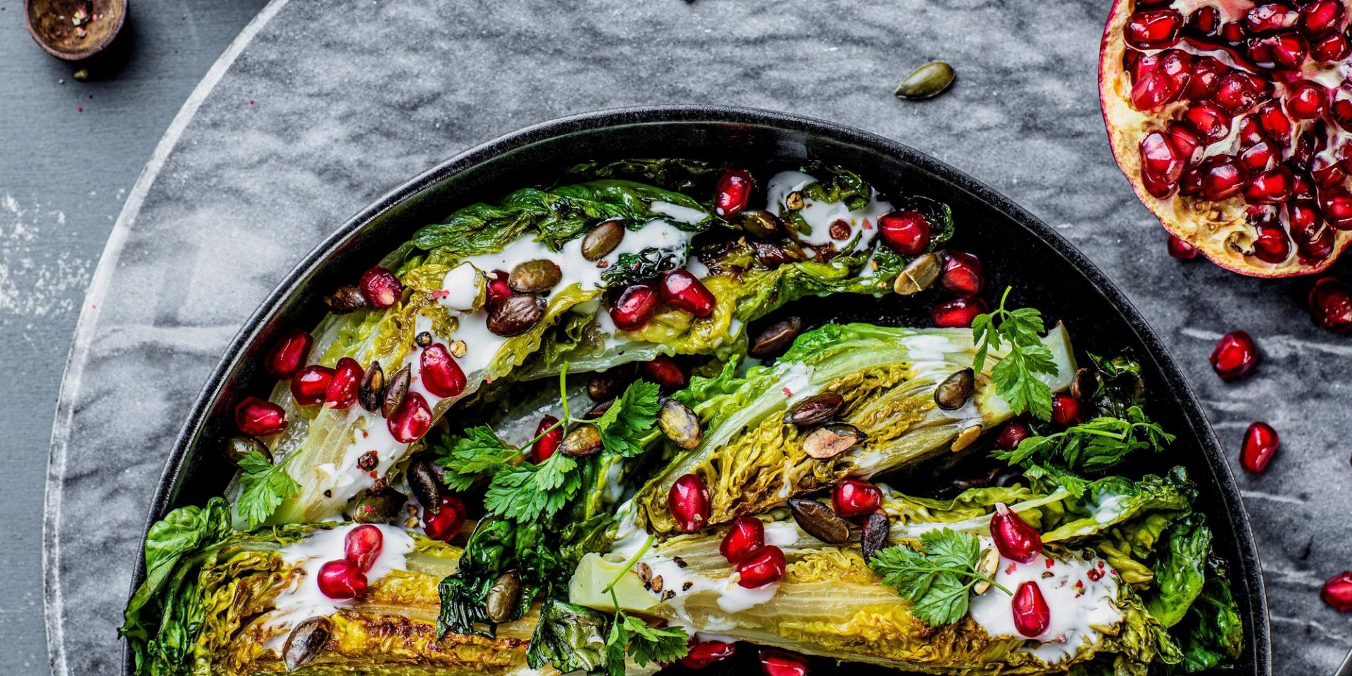 Stekt hjertesalat med kefirdressing, granateplekjerner og gresskarkjerner, servert på fat.