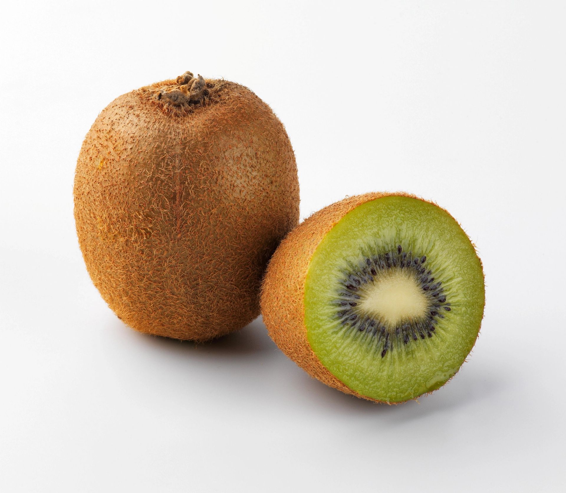 En hel kiwi og en halvert kiwi liggende ved siden av hverandre, med brun, lodden utside og grønt fruktkjøtt med svarte frø