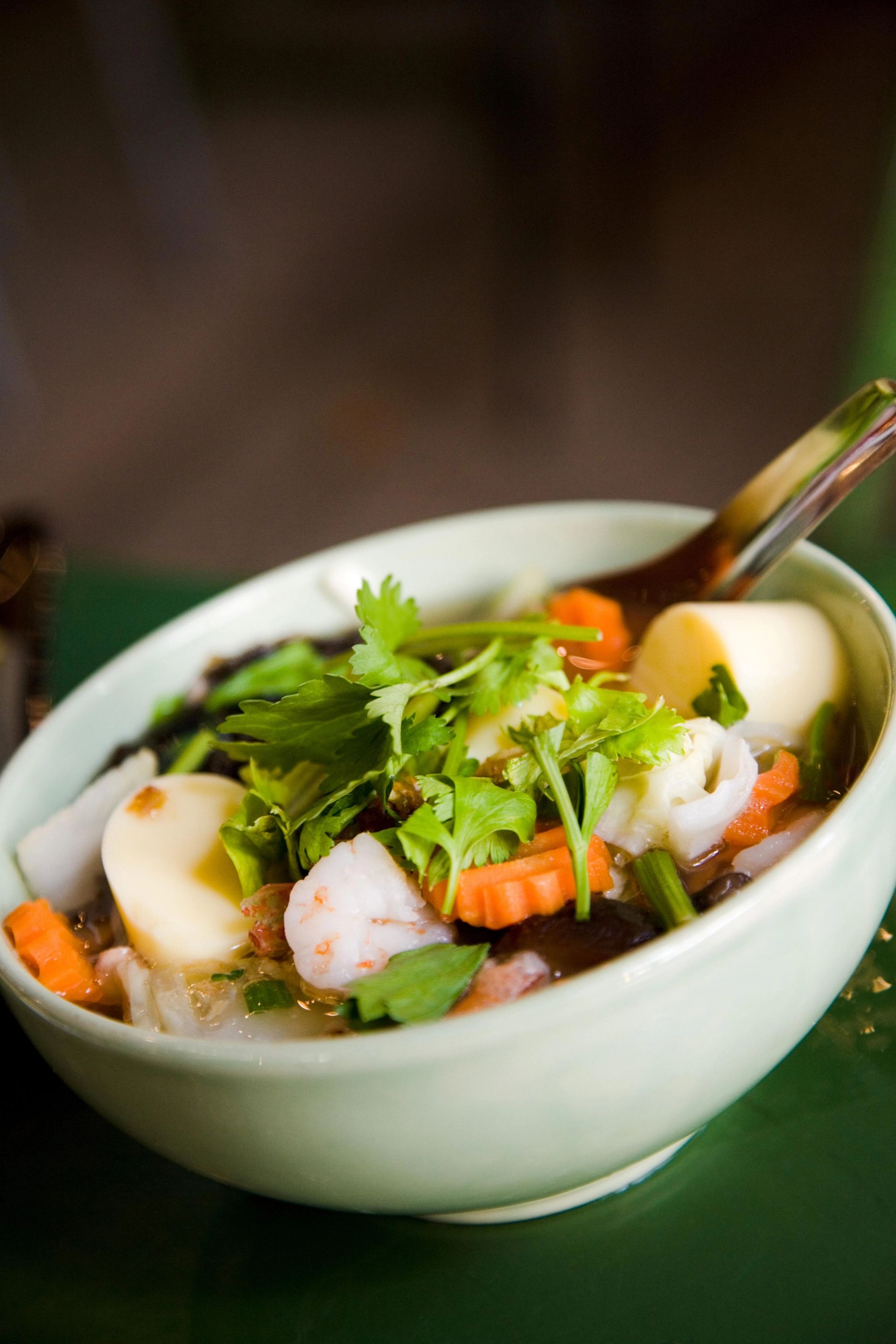 Skål med asiatisk suppe som inneholder kokte egg, reker, gulrøtter, nudler og friske korianderblader, servert med skje.